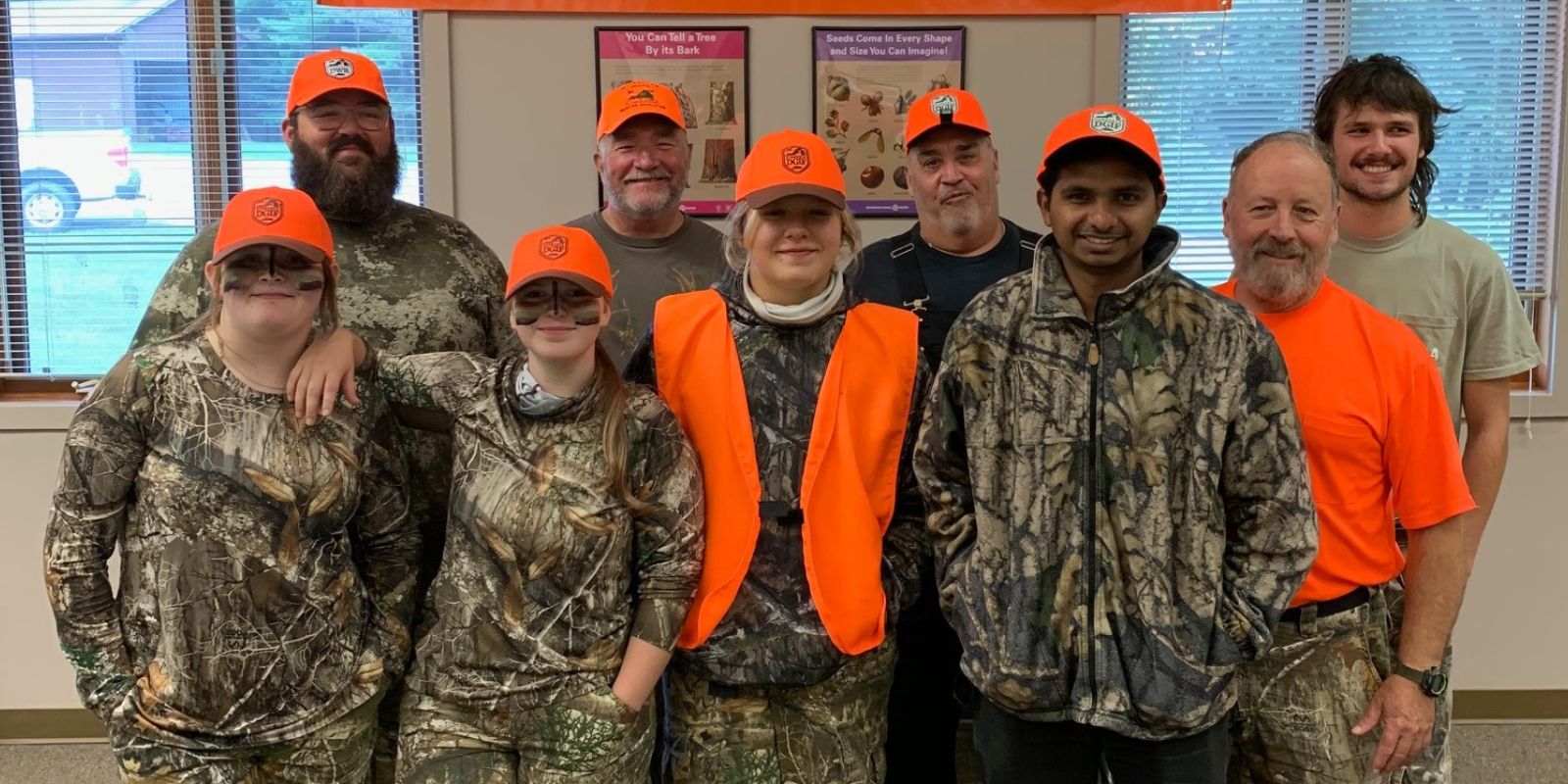 Un grupo de ocho hombres y mujeres de pie juntos, todos vestidos con camuflaje y naranja brillante. 
