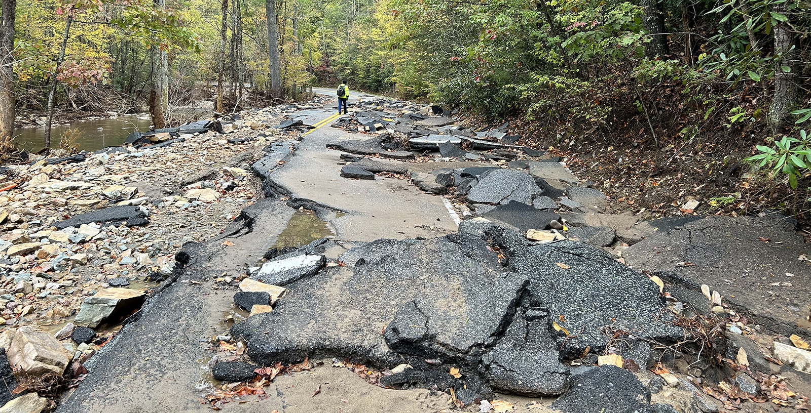 Una foto de una carretera destrozada, con pedazos de asfalto esparcidos alrededor, junto a un arroyo.