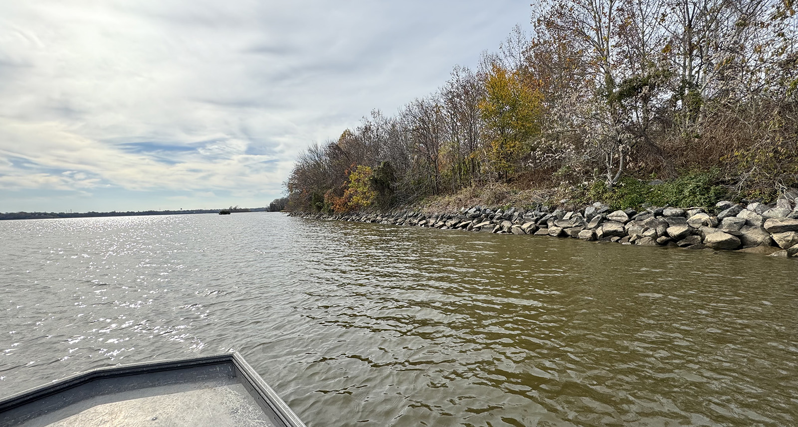 Una foto tomada desde un pequeño bote de la orilla de un río bordeada de grandes rocas rodadas, conocidas como rip-rap.