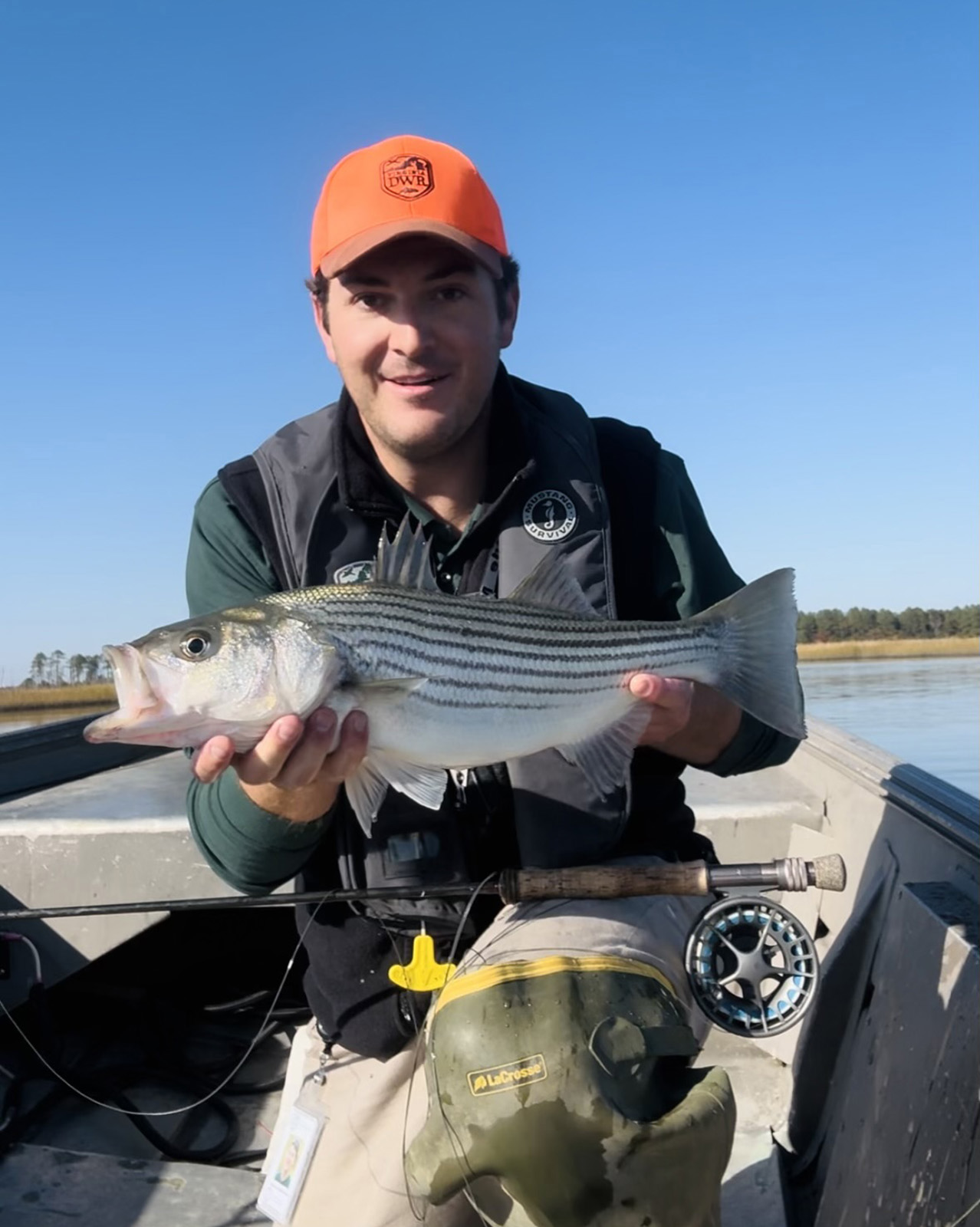 Una foto de un hombre arrodillado en la parte delantera de un pequeño bote, sosteniendo una lubina rayada que atrapó.