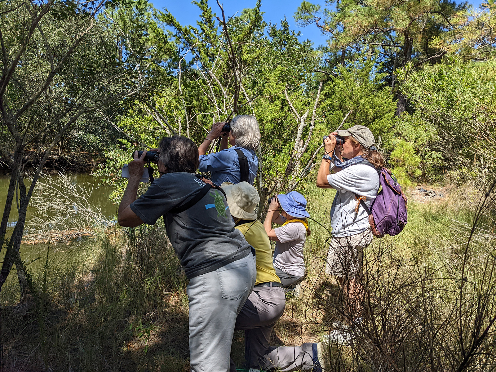 Una foto de un grupo de personas en la orilla de un río, mirando a través de binoculares a través del agua.