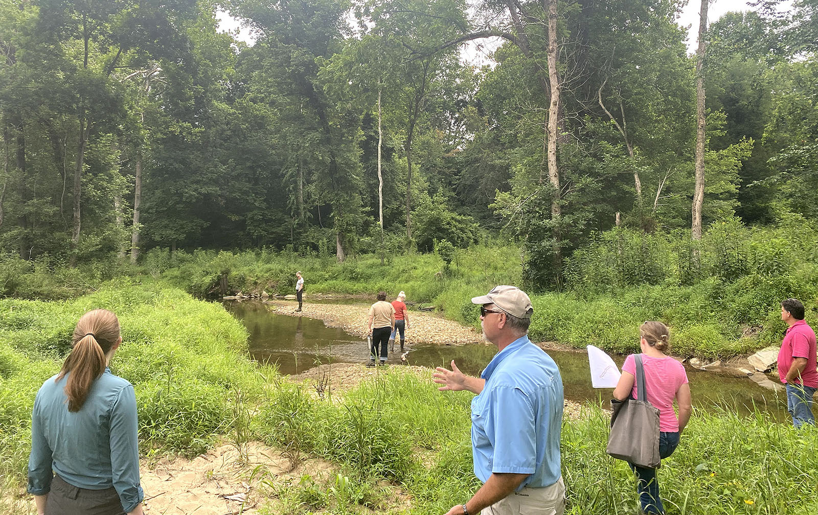 Un grupo de personas se congrega a orillas de un arroyo, en discusión.