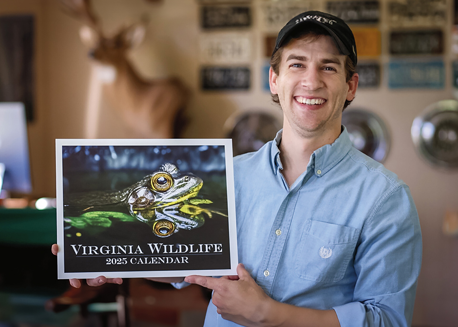 Una foto de un hombre con una amplia sonrisa en su rostro sosteniendo un calendario de Virginia Wildlife con una gran foto de una rana en la portada.