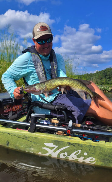 Un hombre en un kayak de pesca sentado en la parte superior sosteniendo un piquero de cadena verde.
