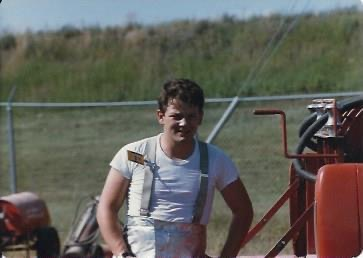 Una foto antigua de un joven con uniforme de bombero de pie junto a un equipo de extinción de incendios.